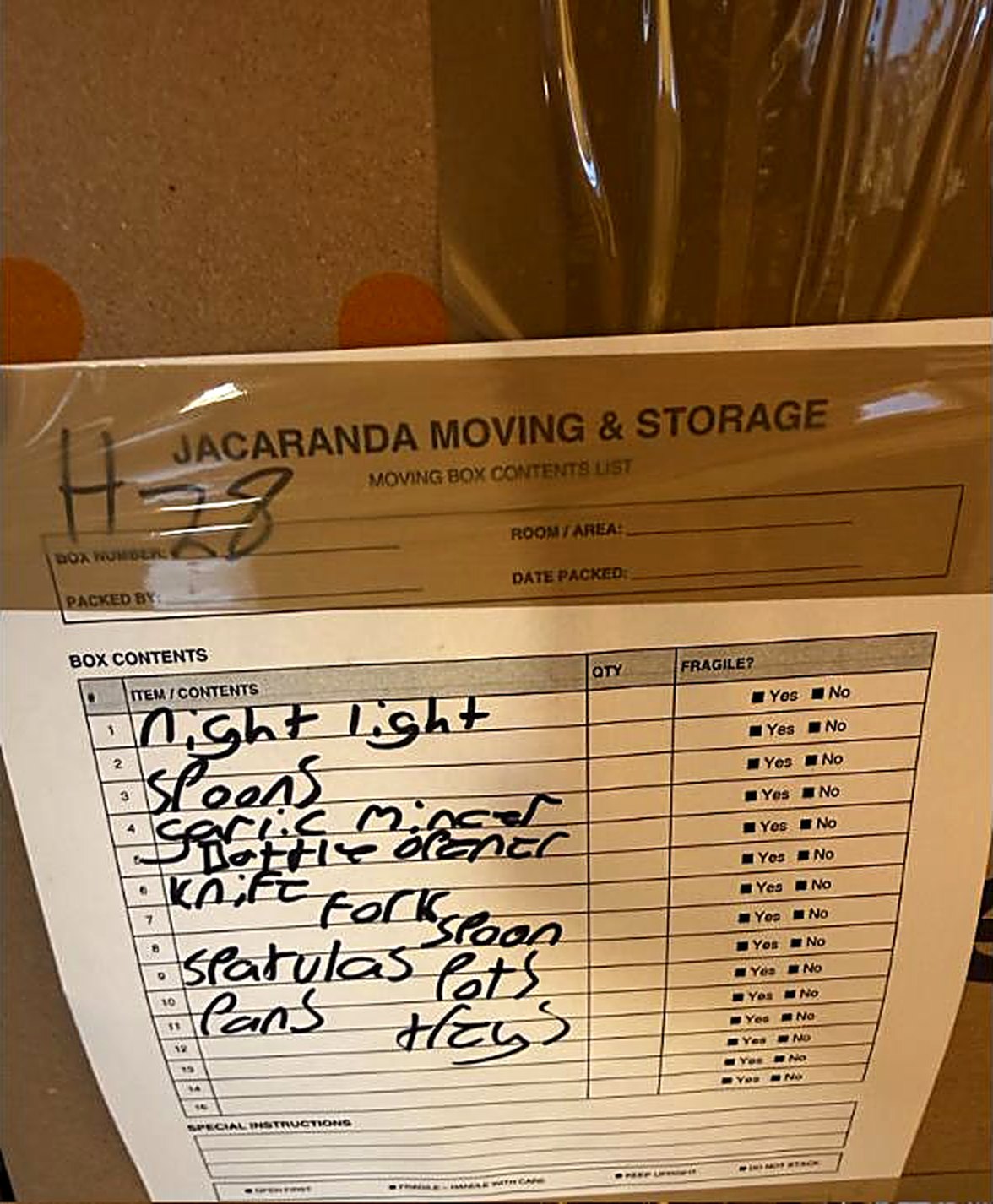 A Jacaranda moving box contents list taped to a packed carton, listing the items inside